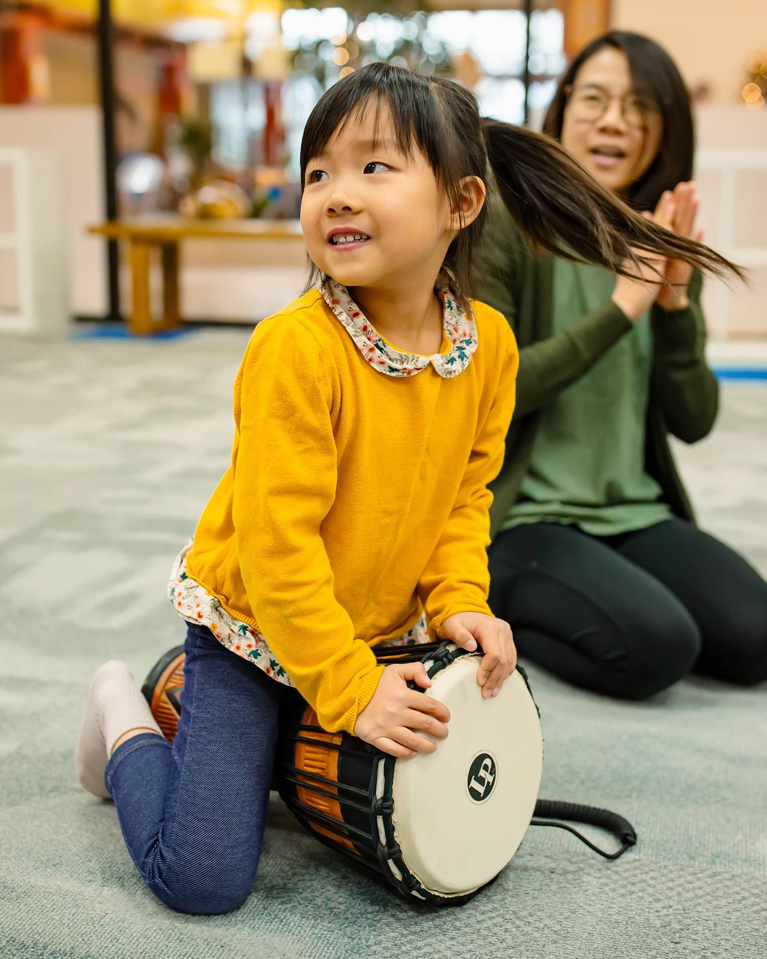 A young child joyfully playing a djembe drum in a Rhythm Kids music class in East Nashville